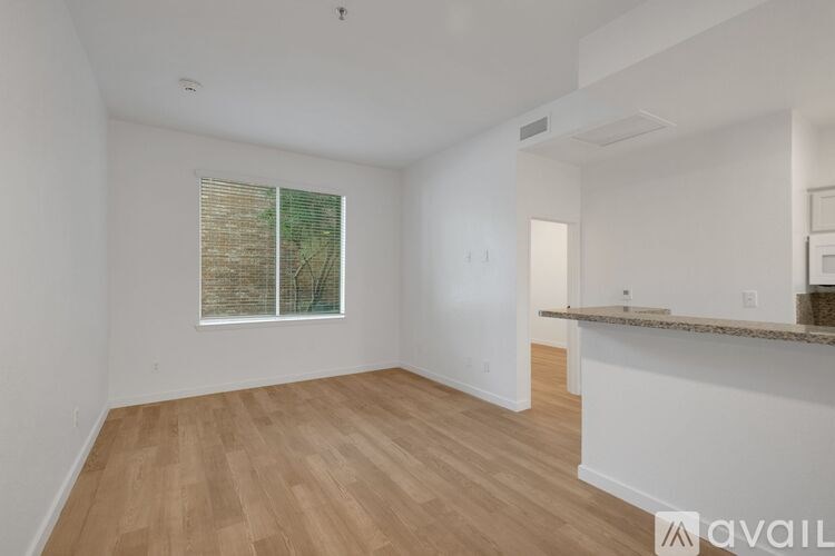 A spacious room with wooden flooring and a window with blinds.