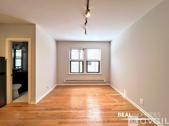 A spacious room with wooden flooring and a window with blinds.