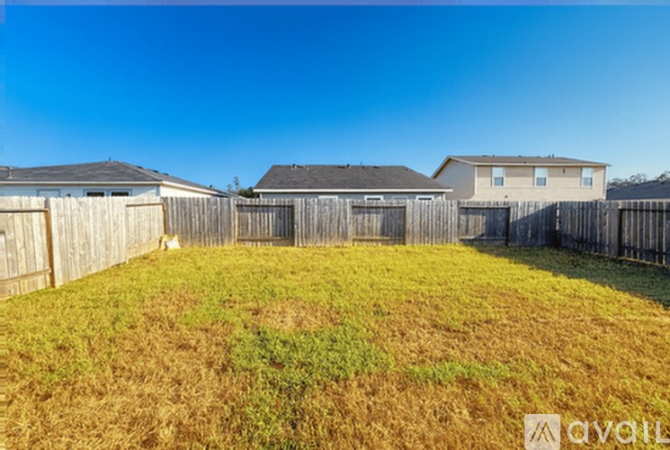 A grassy field with a wooden fence and houses in the background.