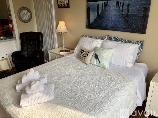 A bedroom with a bed, chair, lamp, and a painting on the wall.