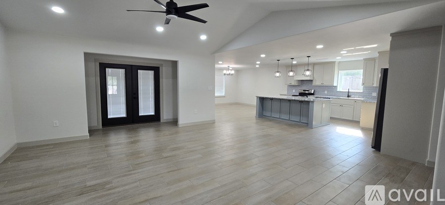 A spacious living room with a kitchen in the background and a ceiling fan above.