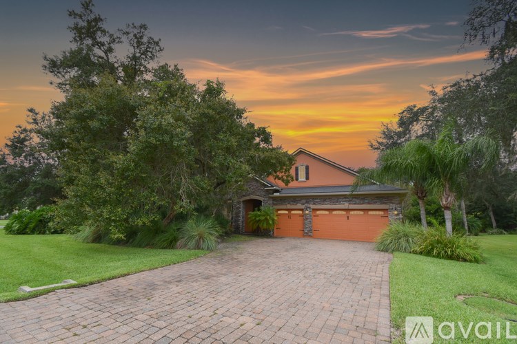 A house with a driveway and a garage is surrounded by greenery and trees.
