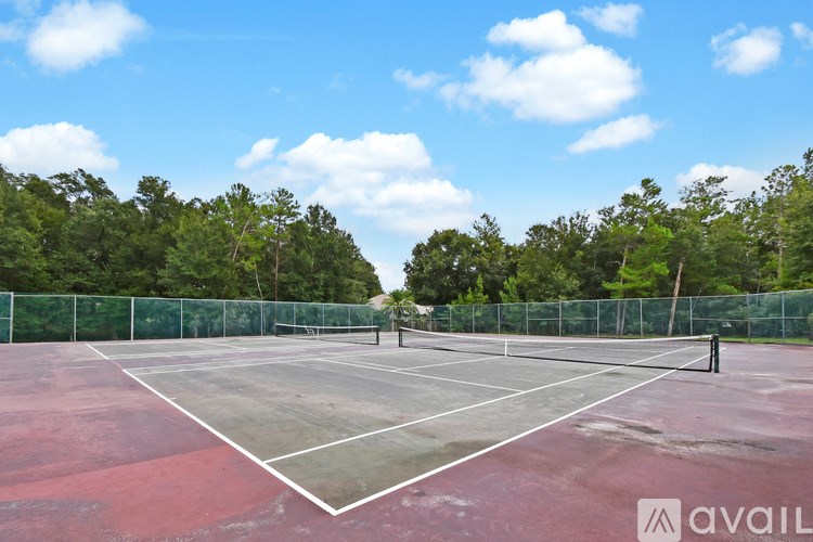 A tennis court surrounded by a green fence and trees.