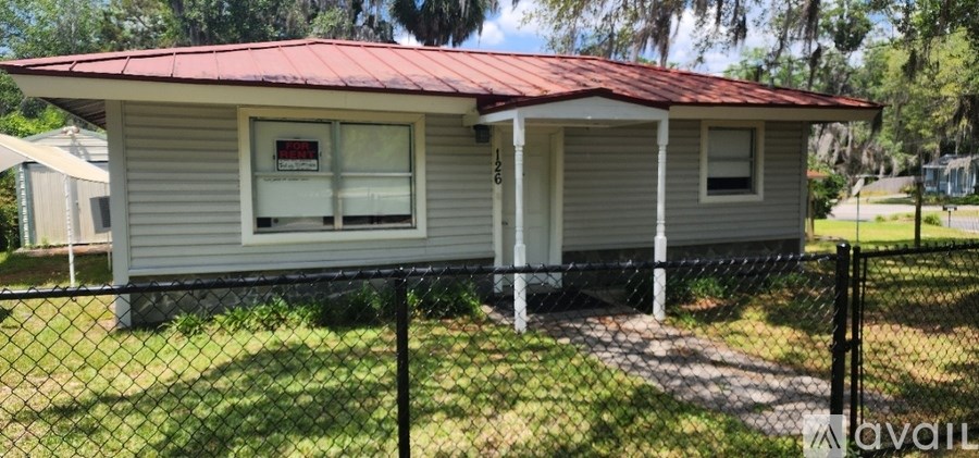 A small house with a red roof is surrounded by a black fence.