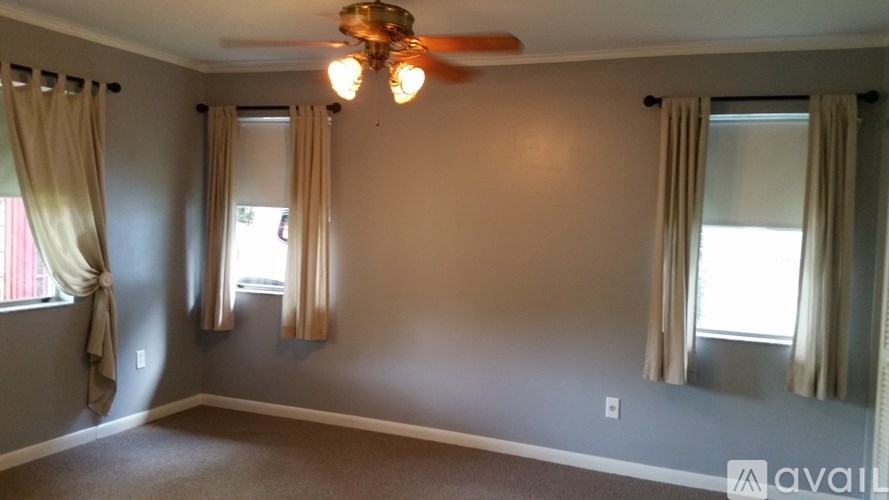 A room with a ceiling fan and two windows with curtains.
