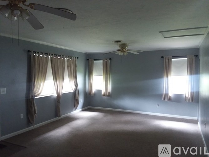 A room with a ceiling fan and two windows with curtains.