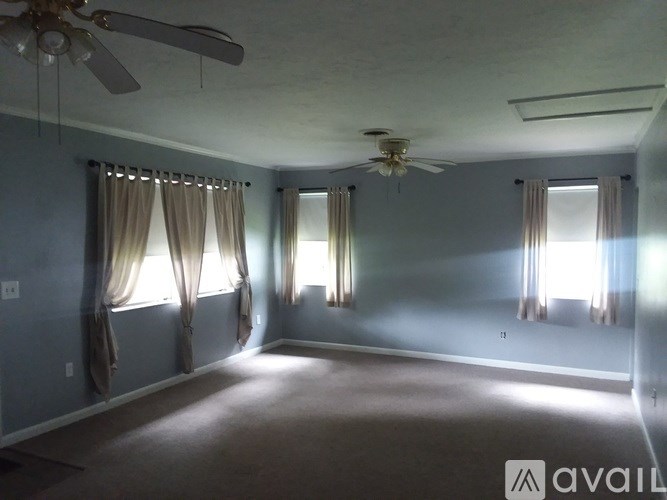 A room with a ceiling fan and two windows with curtains.