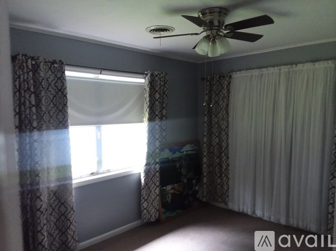 A room with a ceiling fan and a window with curtains.