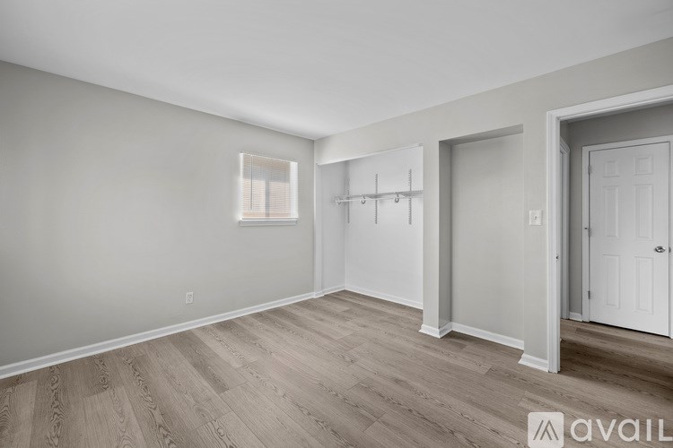 A room with wooden flooring and white walls, with a door on the right and a window on the left.