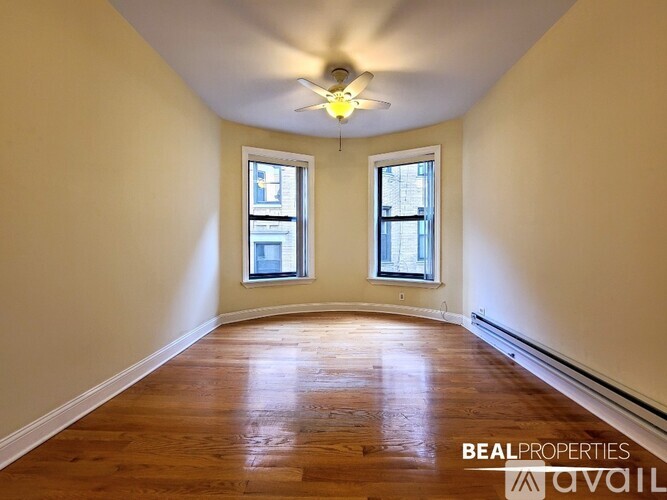 A room with wooden floors and two windows is available for rent.