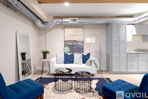 A living room with a white sofa, blue ottoman, and a painting on the wall.
