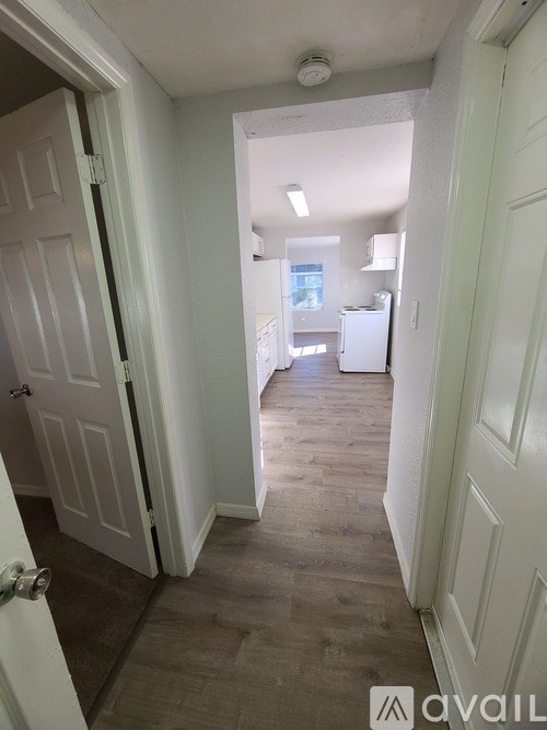 A hallway with a door on the left and a fridge in the distance.