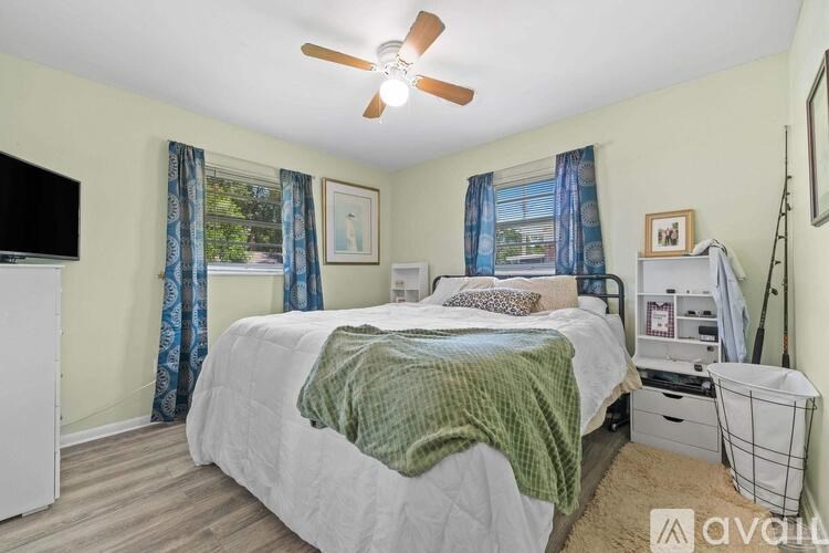 A bedroom with a bed, a ceiling fan, and a window with curtains.