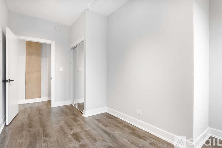 A room with white walls and wooden flooring with a door on the left.