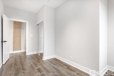 A room with white walls and wooden flooring with a door on the left.
