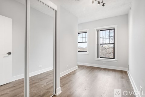 A spacious room with a sliding door, wooden flooring, and a window with a view of bare trees outside.
