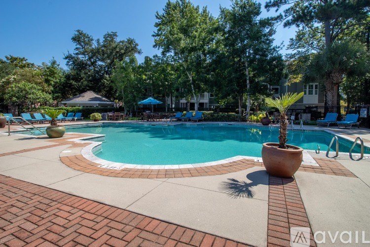 A pool surrounded by trees and a patio area with chairs and a table.