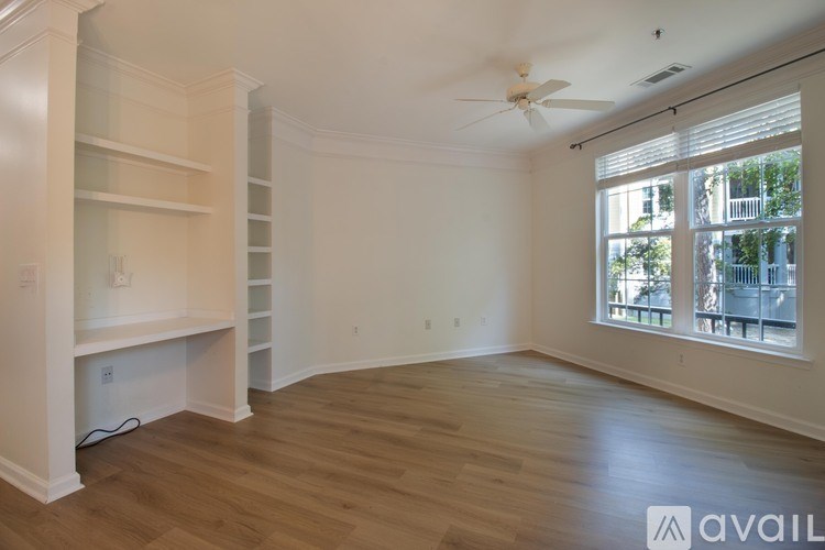 A room with a fan, wooden floors, and a window with a view of a balcony.