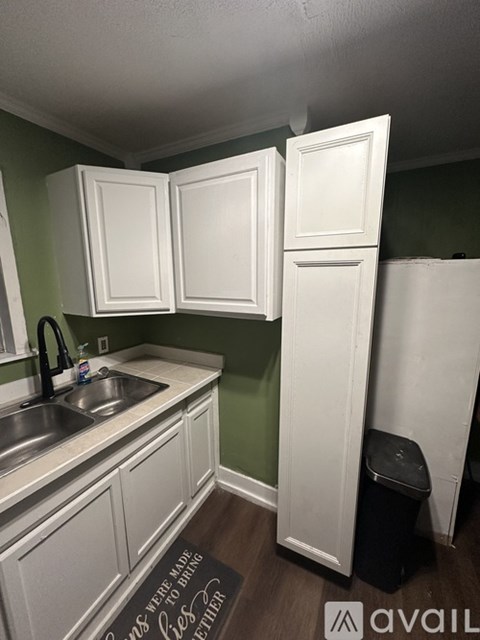 A kitchen with white cabinets and a black trash can.