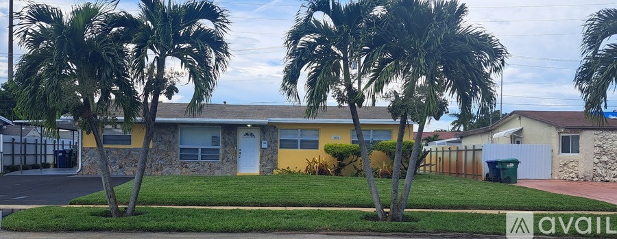 A yellow house with a white door is surrounded by palm trees.