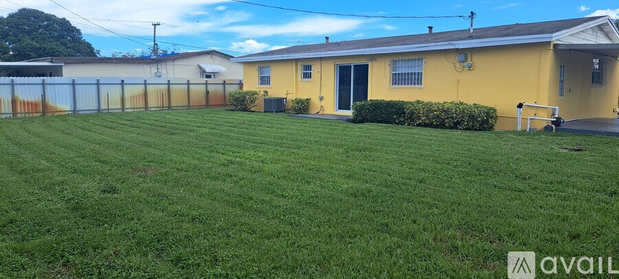 A yellow house with a fence and green lawn in front.
