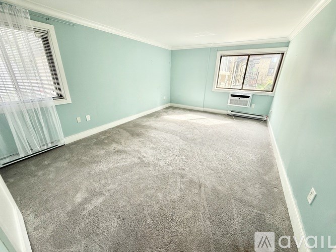 A room with a grey carpet and a window with white curtains.