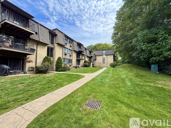 A grassy area in front of apartment buildings with a walkway and a drain in the grass.