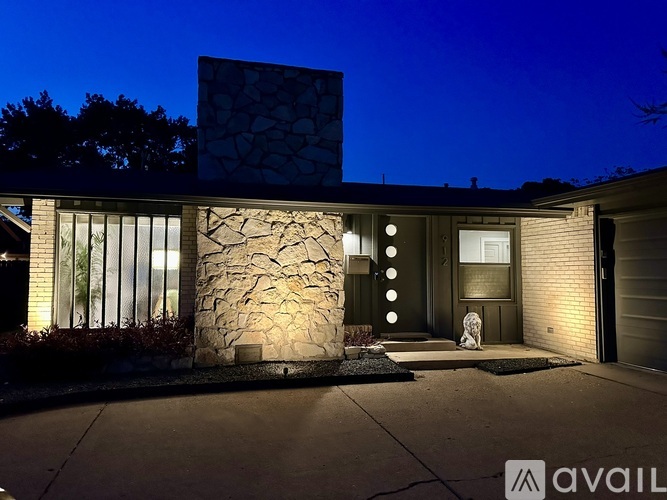 A modern house with a stone wall and glass windows is illuminated at night.