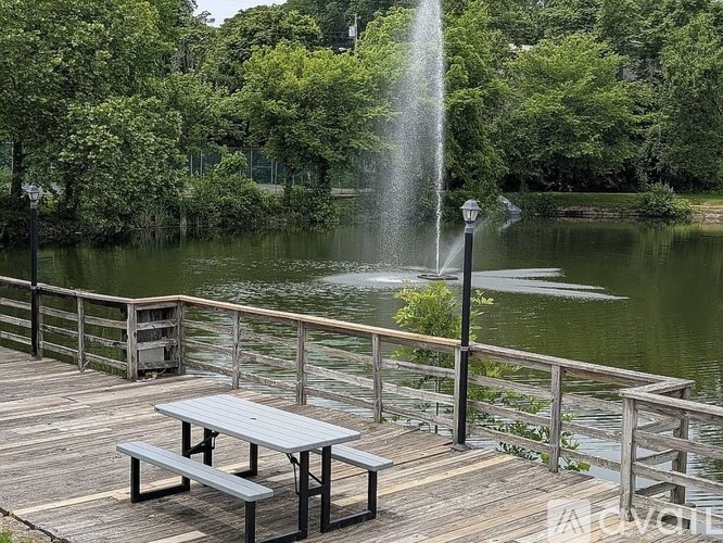 A wooden deck with a table and bench overlooks a pond with a fountain.