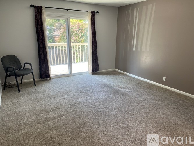 A room with a carpeted floor, a chair, and a sliding glass door leading to a balcony.