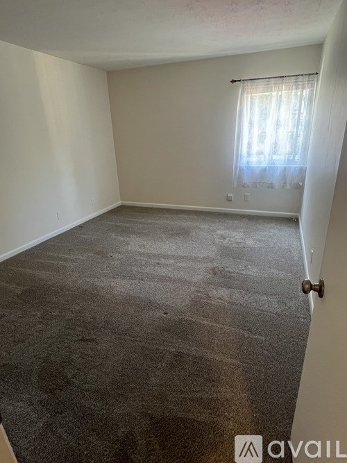 A room with a carpeted floor and a window with curtains.