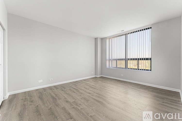 A spacious room with wooden flooring and a window with blinds.