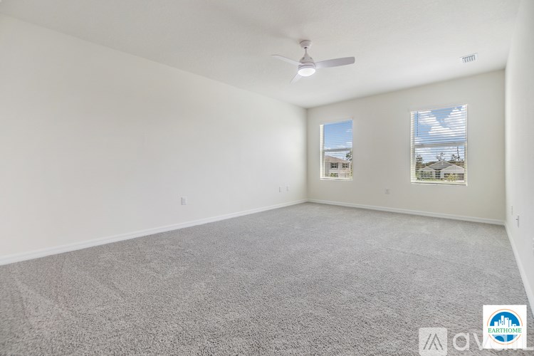 A spacious room with a ceiling fan and two windows.