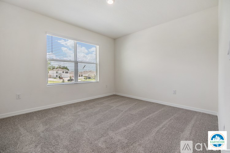 A well lit empty room with a carpeted floor and a window with blinds.