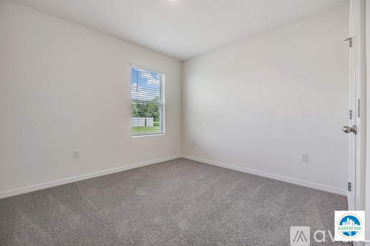 A room with a carpeted floor and a window showing a view of a green lawn and trees.
