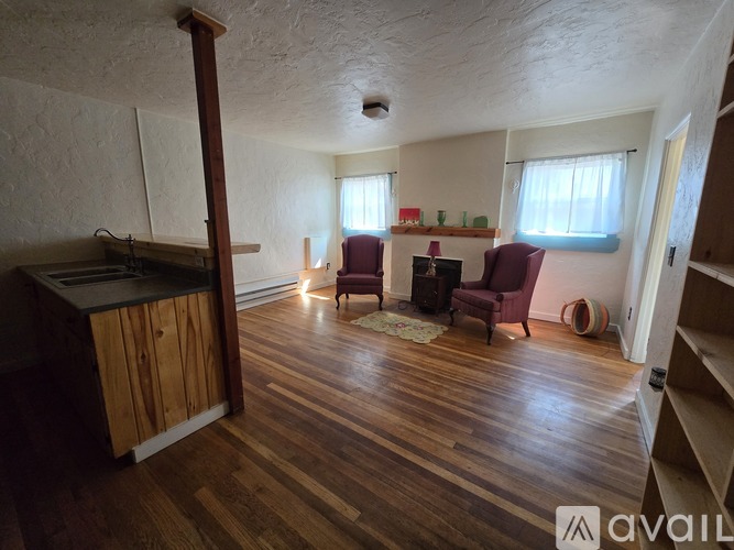 A living room with wooden floors and a kitchen area to the left.