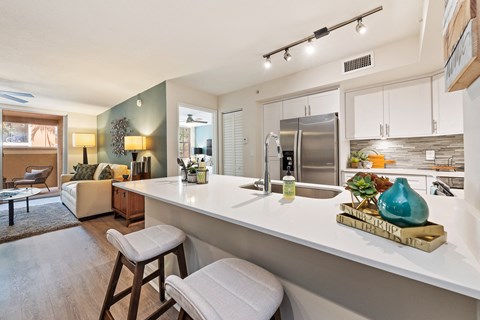 a kitchen with white counter tops and stools and a living room