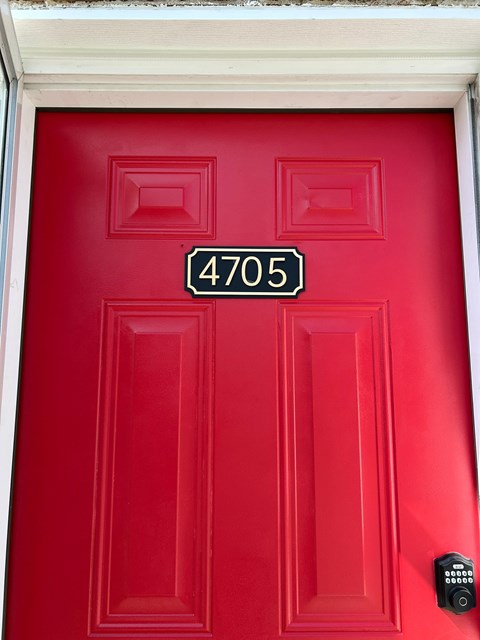 A red door with a black lock and a number plate reading 4705.