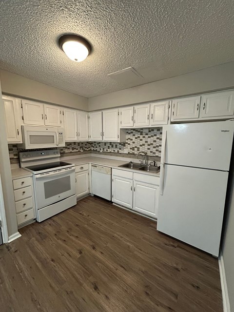 A kitchen with white cabinets and a wooden floor.
