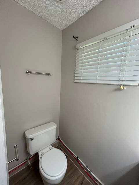 A white toilet in a small bathroom with a towel rack and a window with blinds.