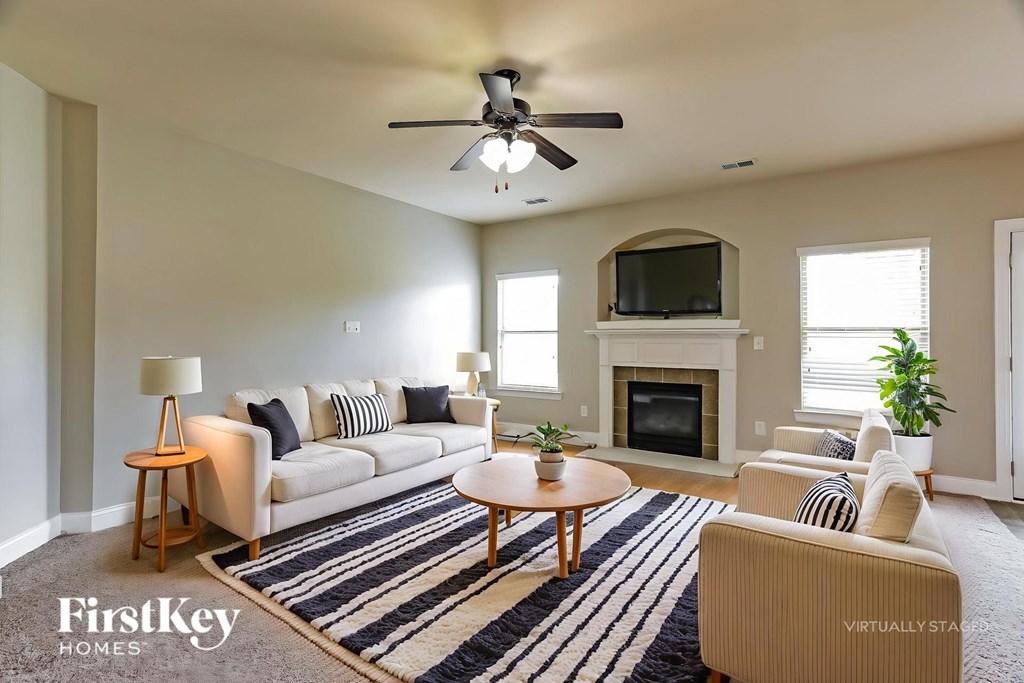 A living room with a fireplace, a couch, a chair, a table, a floor lamp, and a ceiling fan.