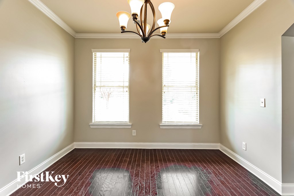 A room with a chandelier, two windows, and a wooden floor.