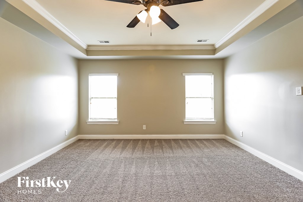 A spacious room with a ceiling fan and two windows.