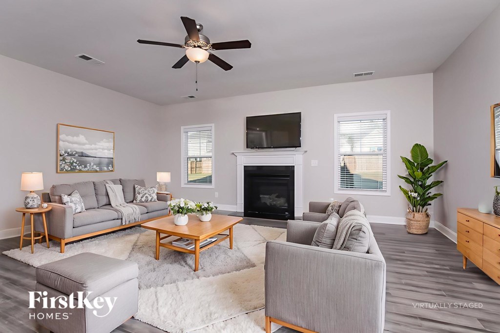 A living room with a grey couch, a coffee table, a fireplace, and a ceiling fan.
