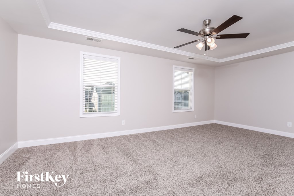 A spacious room with a ceiling fan and two windows.