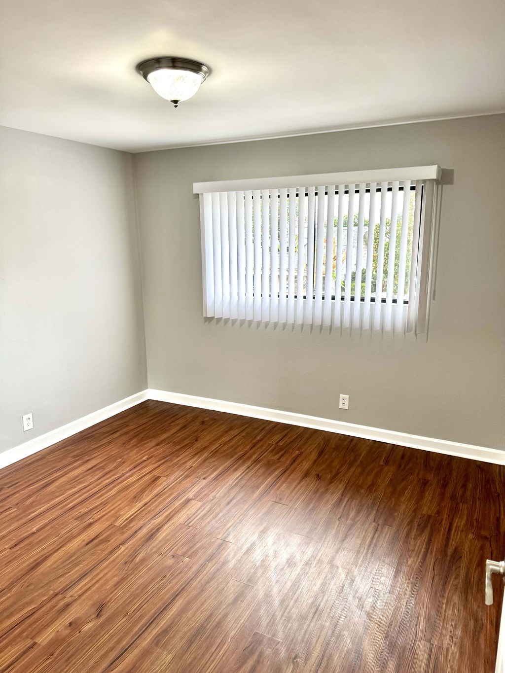 A room with wooden flooring and a window with blinds.