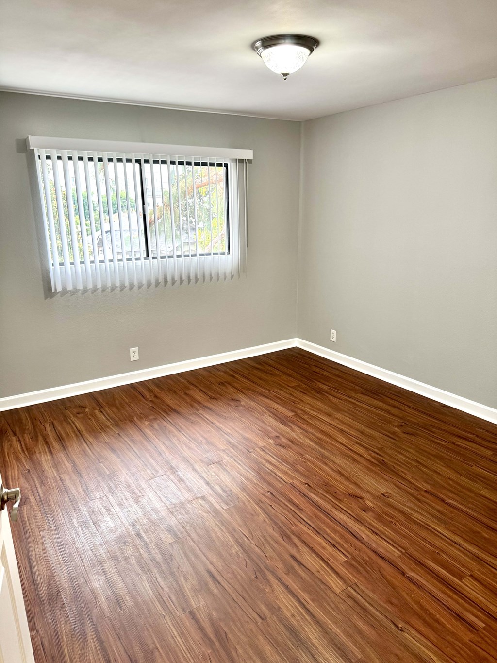 A room with wooden flooring and a window with blinds.