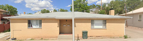 A small house with a brown brick exterior and a green trash can in front.