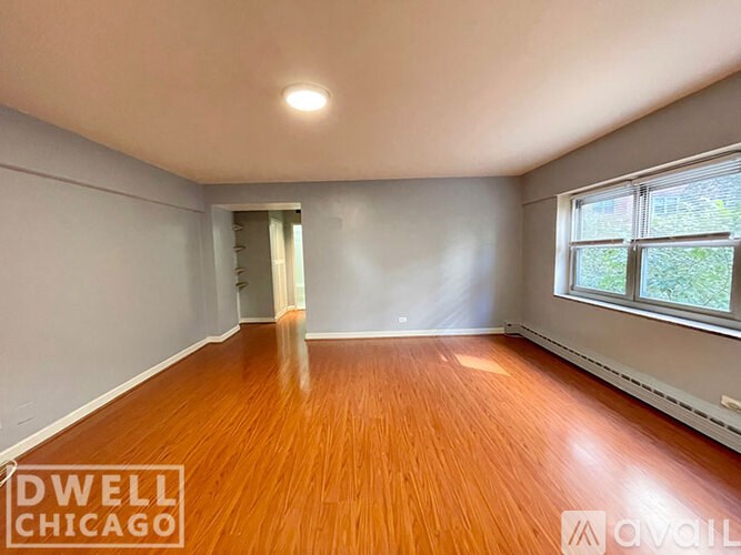 A room with wooden flooring and a window with a view of greenery outside.