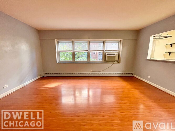 A room with wooden floors and a window overlooking a building.